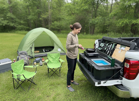 Person setting up a camping area with a tent, chairs, and a portable stove in the back of a truck.